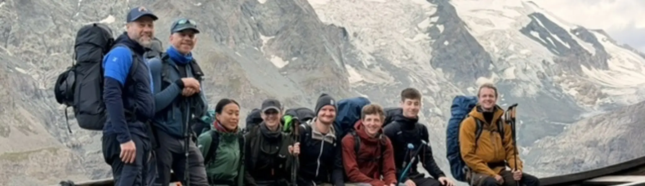 Gruppe von Bergsteigenden mit Rucksäcken und Hochtourenausrüstung an einem Aussichtspunkt vor einer Gletscherlandschaft und schroffen Berggipfeln. | © P.J.Müller