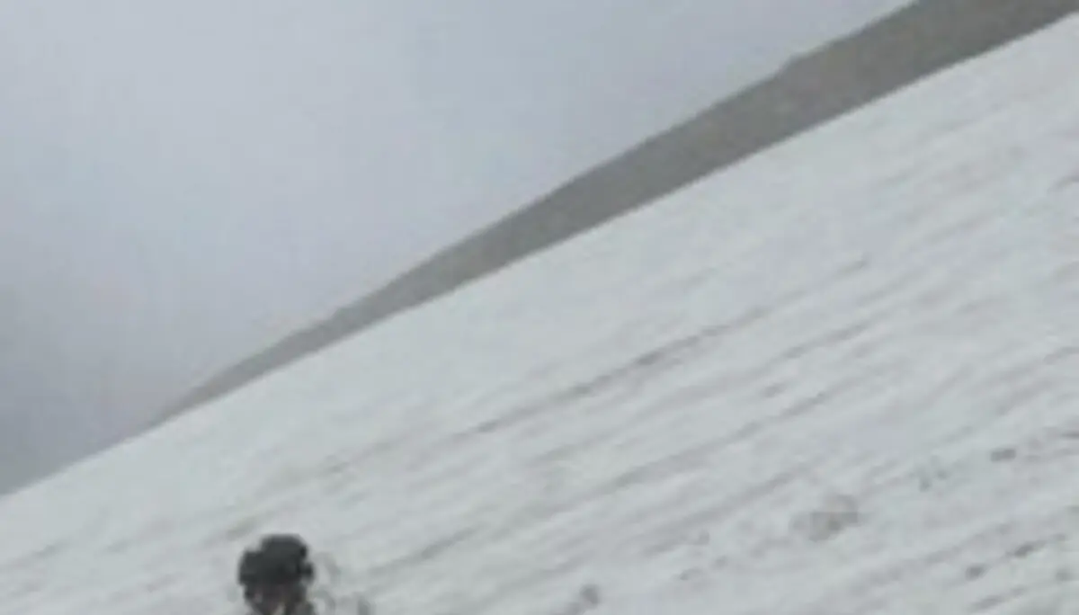 Person sitzt auf einem verschneiten Hang und übt den Einsatz eines Eispickels im Schnee. Die Aufnahme zeigt eine Übung zur Fortbewegung oder Selbstsicherung im winterlichen Hochgebirge. | © P.J.Müller