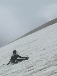 Person sitzt auf einem verschneiten Hang und übt den Einsatz eines Eispickels im Schnee. Die Aufnahme zeigt eine Übung zur Fortbewegung oder Selbstsicherung im winterlichen Hochgebirge. | © P.J.Müller