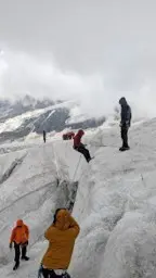Mehrere Personen mit Hochtourenausrüstung üben auf einem Gletscher den Umgang mit Eis und Sicherungstechniken. Eine Person bewegt sich über eine Eisformation, während andere die Übung beobachten. | © P.J.Müller