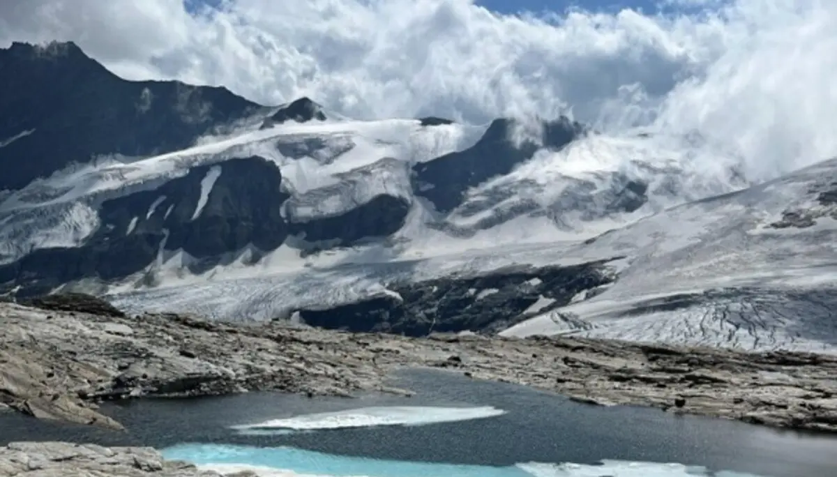 Bergsee vor einer Gletscherlandschaft mit schneebedeckten Gipfeln und Wolken. Felsiger Untergrund umgibt das Wasser in hochalpiner Umgebung. | © P.J.Müller