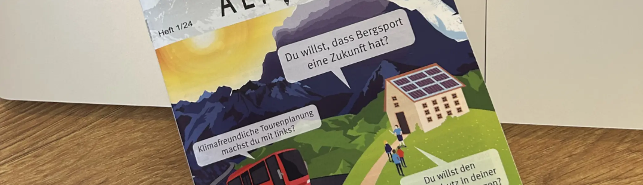 Ein Magazin mit dem Titel „Bielefeld Alpin“ liegt auf einer Laptop-Tastatur. Auf dem Cover ist eine farbige Illustration mit Bergen, einer Seilbahn, einem Haus mit Solaranlage und Wandernden zu sehen. Mehrere Sprechblasen enthalten Texte zu Klimaschutz und nachhaltigem Bergsport. Oben rechts steht das Logo „DAV – Deutscher Alpenverein Sektion Bielefeld“. | © Nicole Laska