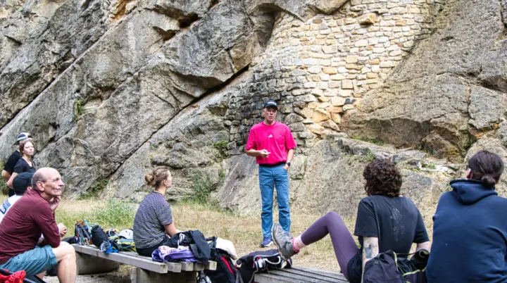 Mehrere Personen sitzen und stehen am Fuß einer Felswand und hören einer Einführung im Klettergebiet zu. | © Thorsten Neuenbäumer