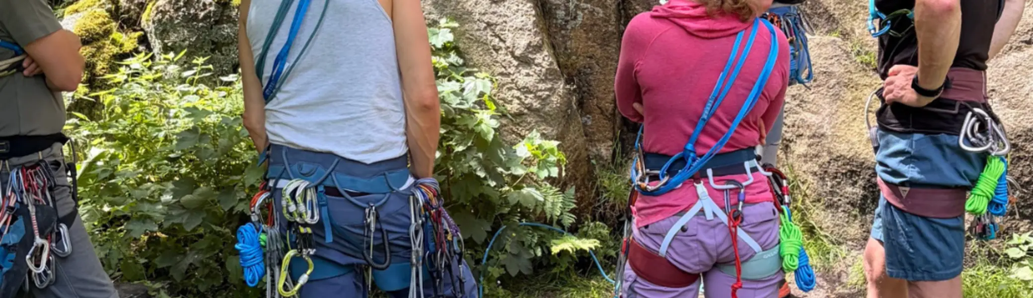 Gruppe von Personen mit Kletterausrüstung steht am Fuß einer Felswand und betrachtet den Aufbau eines Sicherungsstandes mit Seilen und Karabinern. | © Gunnar Helms