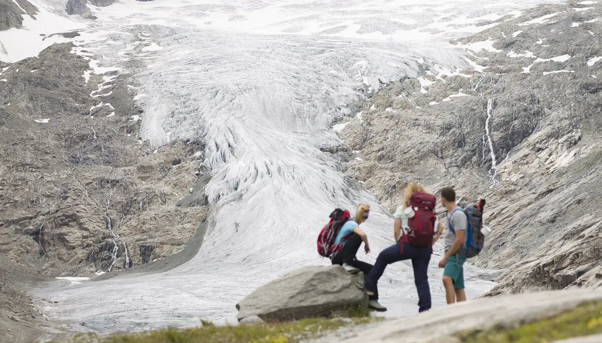 Drei Wandernde blicken nahe der Neuen Prager Hütte am Großvenediger auf den verschwindenden Gletscher. | © DAV / Jens Klatt